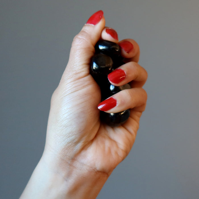 hand holding a bunch of tumbled jet stones