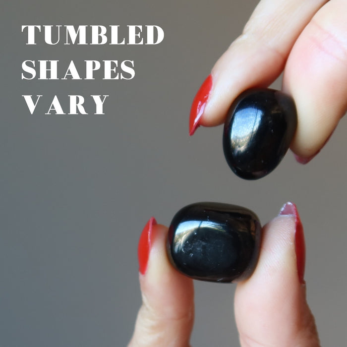 fingers holding two jet stones showing tumbled shapes vary