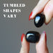 fingers holding two jet stones showing tumbled shapes vary