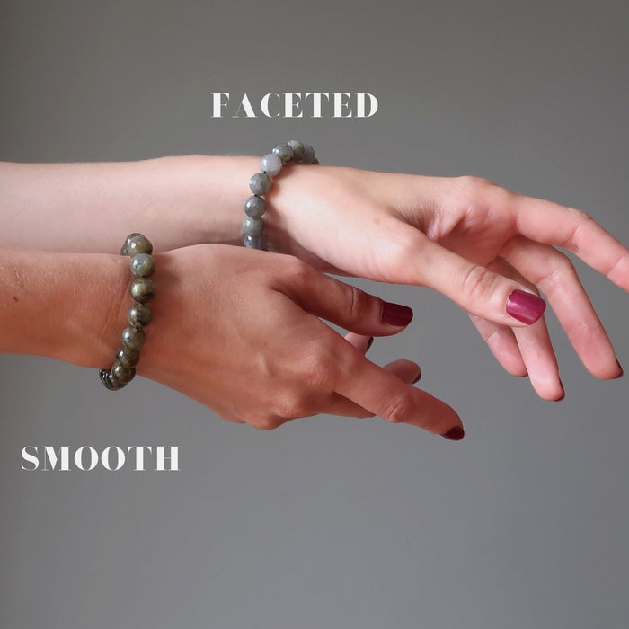 pair of hands, one wearing faceted and one wearing smooth labrdorite bracelet