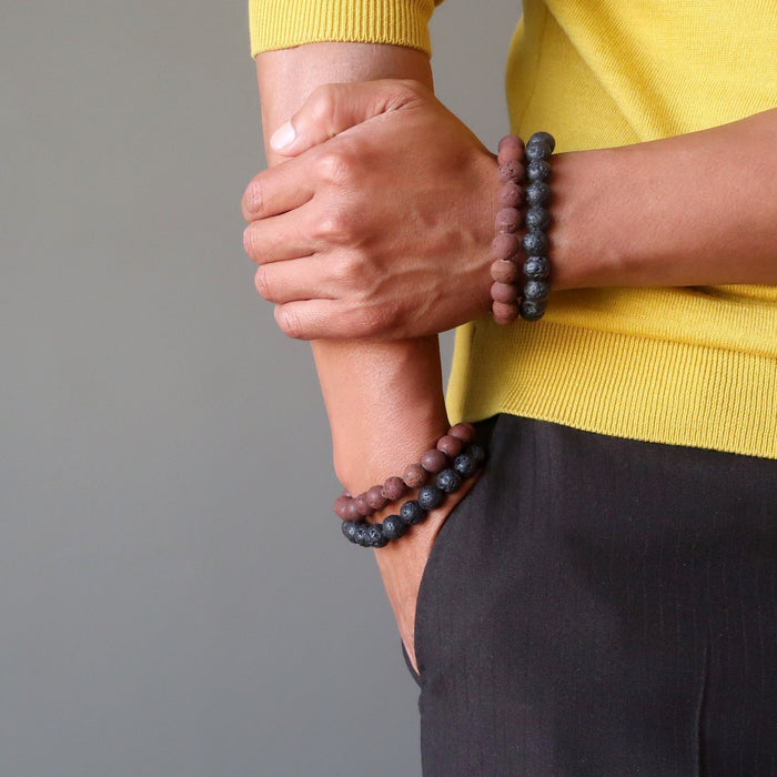 man with hand in the pocket and the other on his forearm both wearing red and black lava bracelets