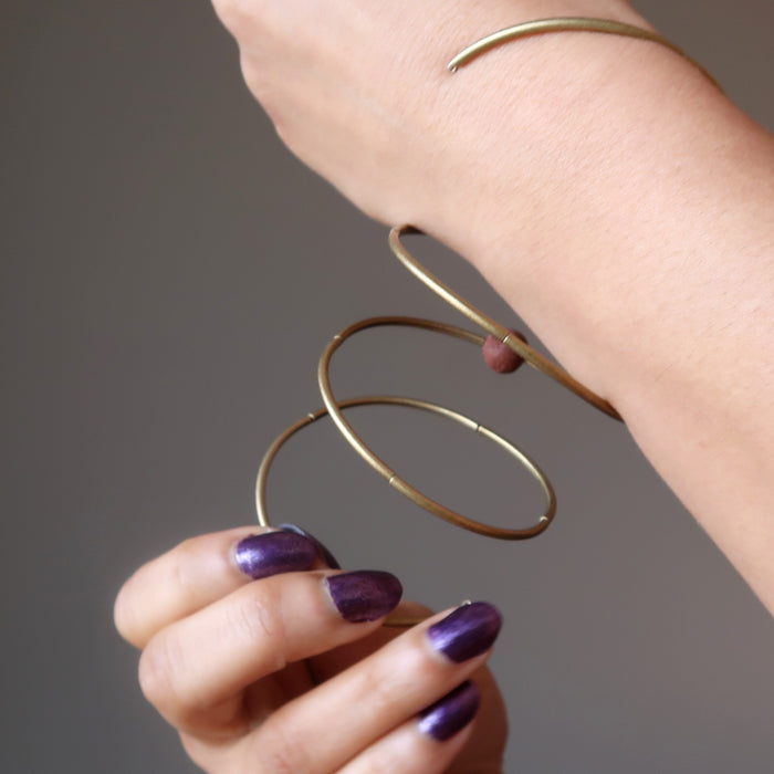 hand coiling round red lava bead on 3 coils of antique gold memory wire bracelet around the wrist