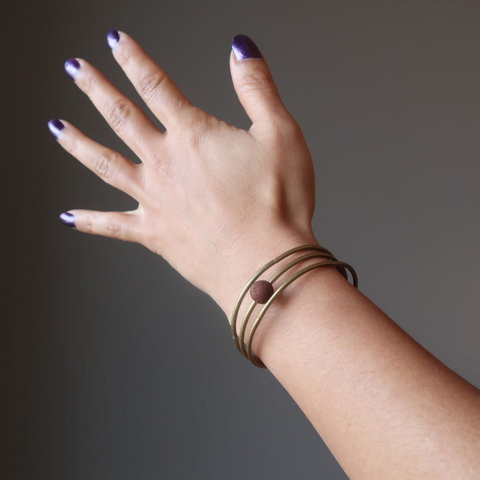 female hand modeling round red lava bead on 3 coils of antique gold memory wire bracelet