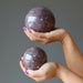 pair of hands holding purple lepidolite spheres in each palm