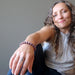 Aleks of Satin Crystals sits casually smiling while wearing a purple lepidolite bracelet that was hand made at satin crystals