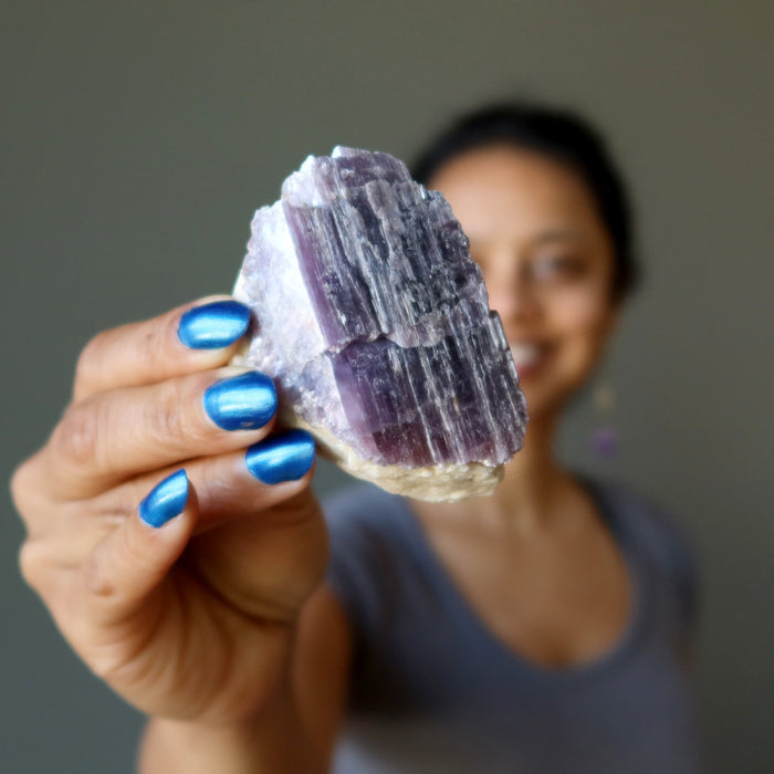 hand holding rough purple lepidolite on white quartz cluster