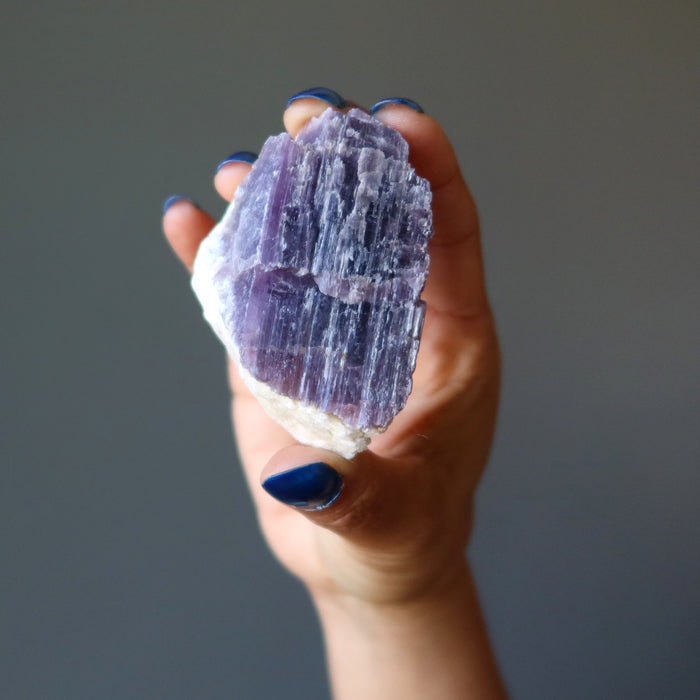 hand holding rough purple lepidolite on white quartz cluster