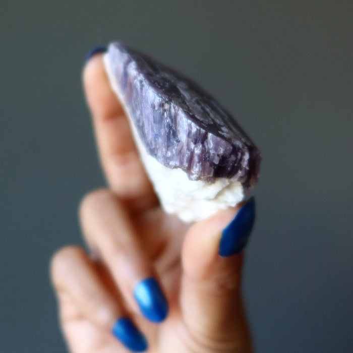 hand holding rough purple lepidolite on white quartz cluster