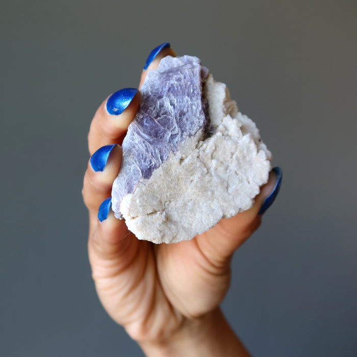 hand holding rough purple lepidolite on white quartz cluster