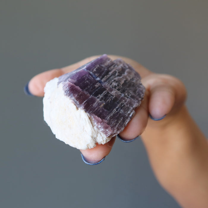 hand holding rough purple lepidolite on white quartz cluster
