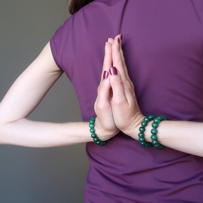 female model with hands in prayer at her back wearing three green malachite stretch bracelets