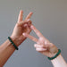 man and woman's hands making peace signs wearing green malachite bracelets