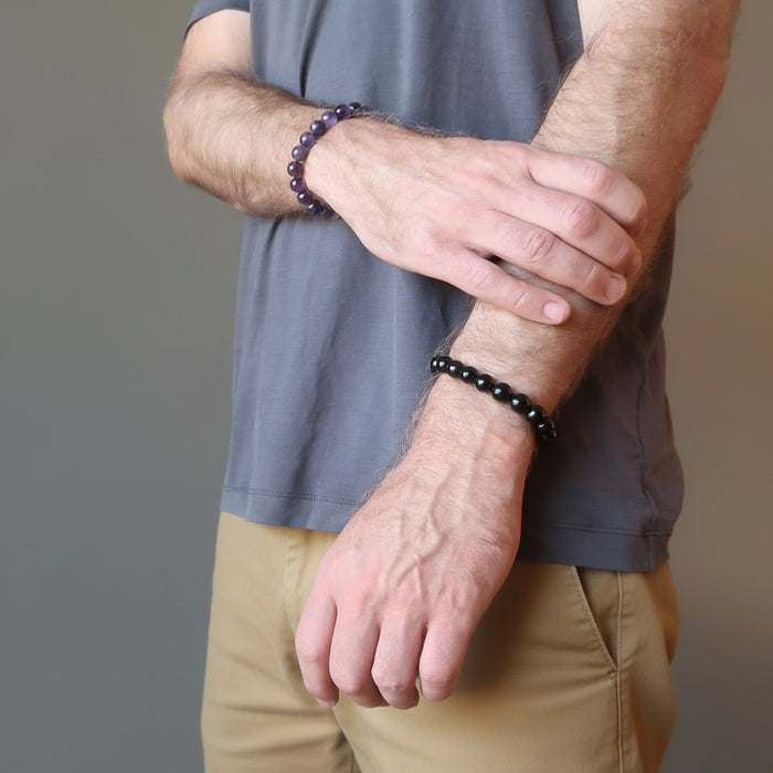 man wearing amethyst bracelet on one wrist and black tourmaline bracelet on the other