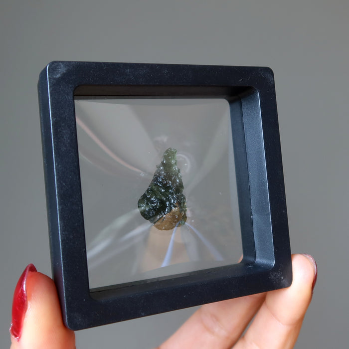hand holding up a moldavite in a suspension display case