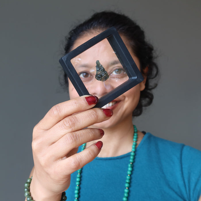 sheila of satin crytals holding up a moldavite in a suspension display case