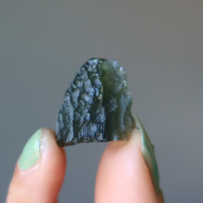 hand holding up a rough moldavite gemstone