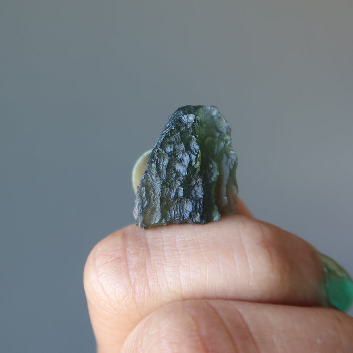hand holding up a rough moldavite gemstone