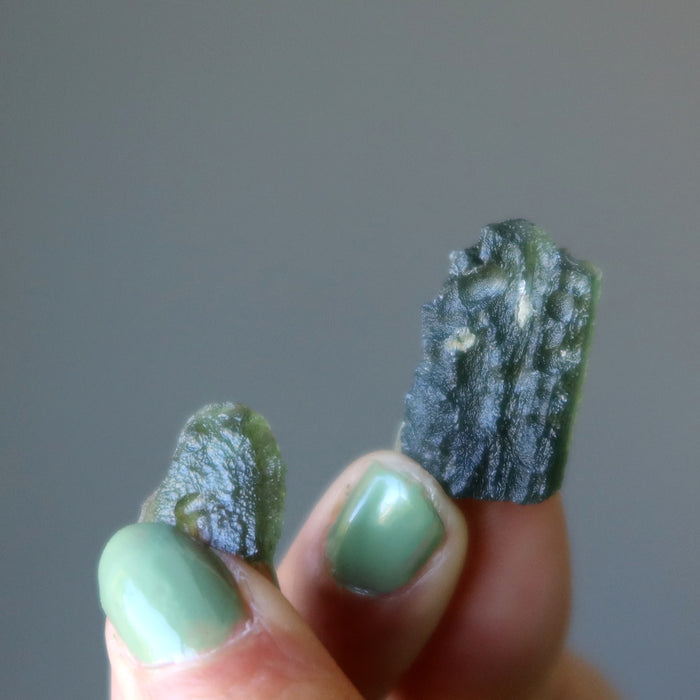 hand holding up 2 rough moldavite gemstones