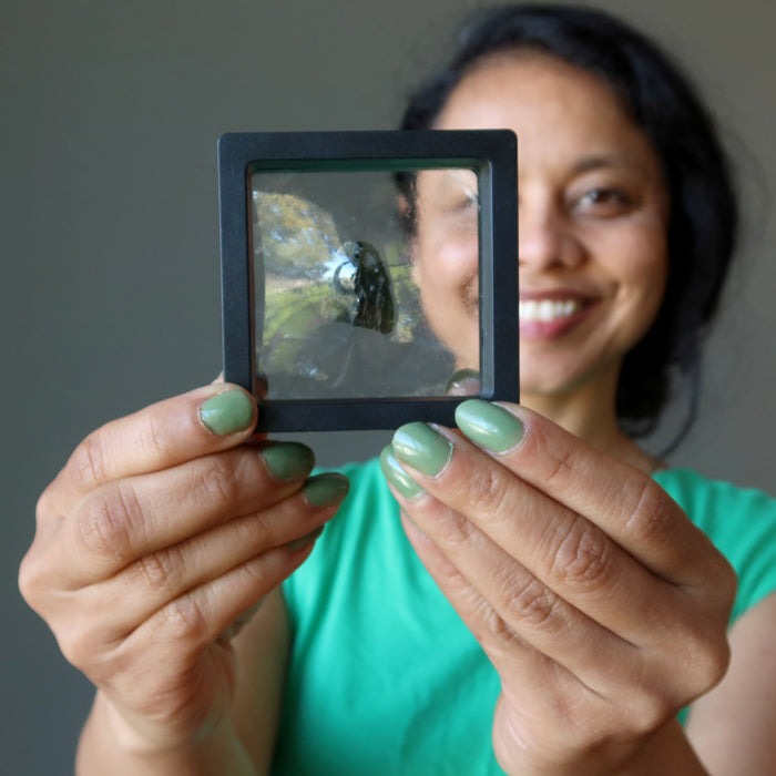 hand holding up a rough moldavite gemstone in a display case