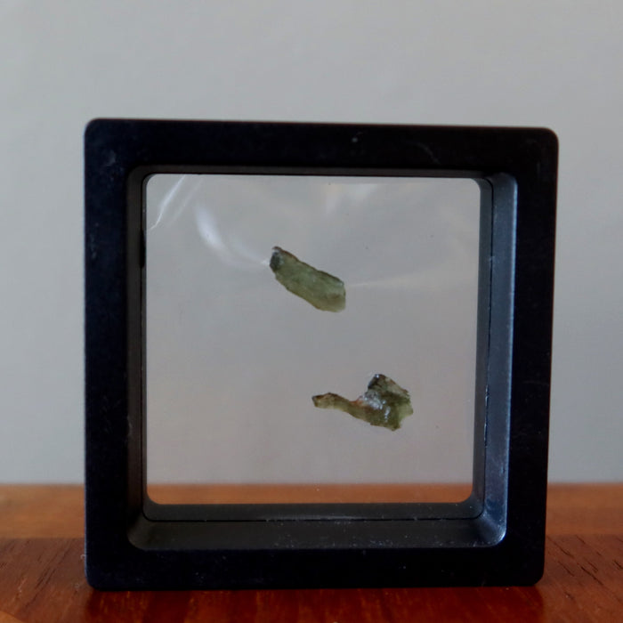 2 rough green moldavite gemstones in suspension display case