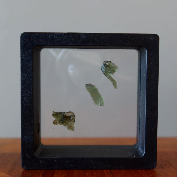 3 rough green moldavite gemstones in suspension display case