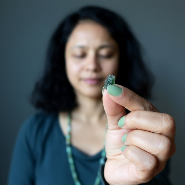 sheila of satin crystals holding rough green moldavite gemstone