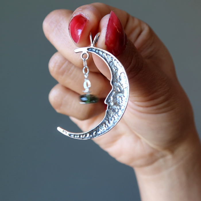 hand holding sterling silver crescent moon with faceted green moldavite pendant showing back