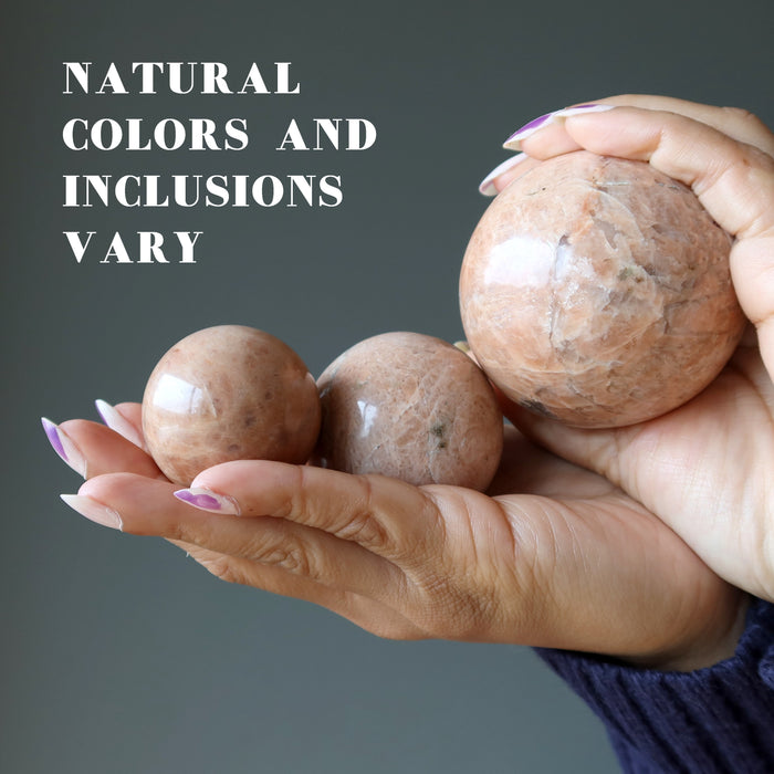 hand holding three peach moonstone spheres to show natural colors and inclusions vary