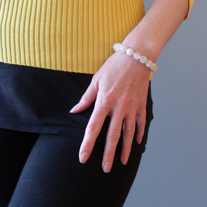 woman's hand at hip wearing white rainbow moonstone beaded stretch bracelet
