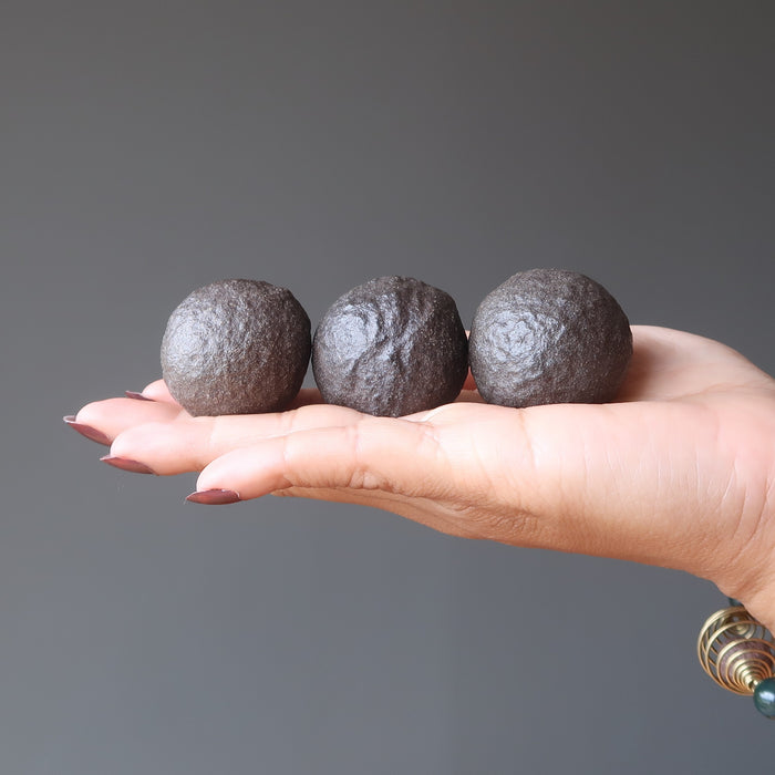 hand holding three brown moqui marble stones