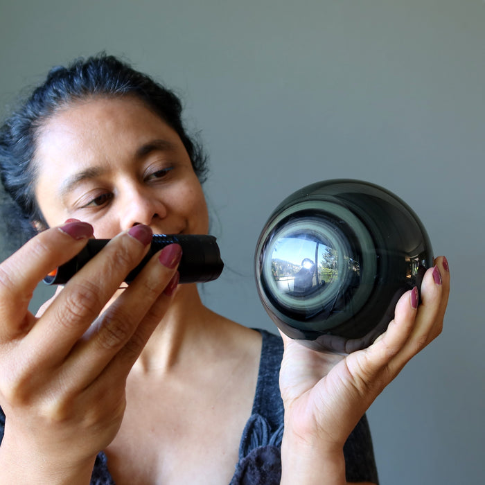 woman using flashlight to shine on rainbow obsidian sphere