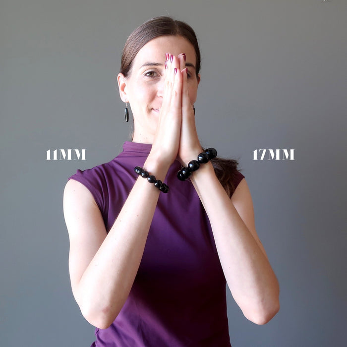 lucia of satin crystals with hands in prayer wearing a 11mm and a 17mm rainbow obsidian beaded stretch bracelet