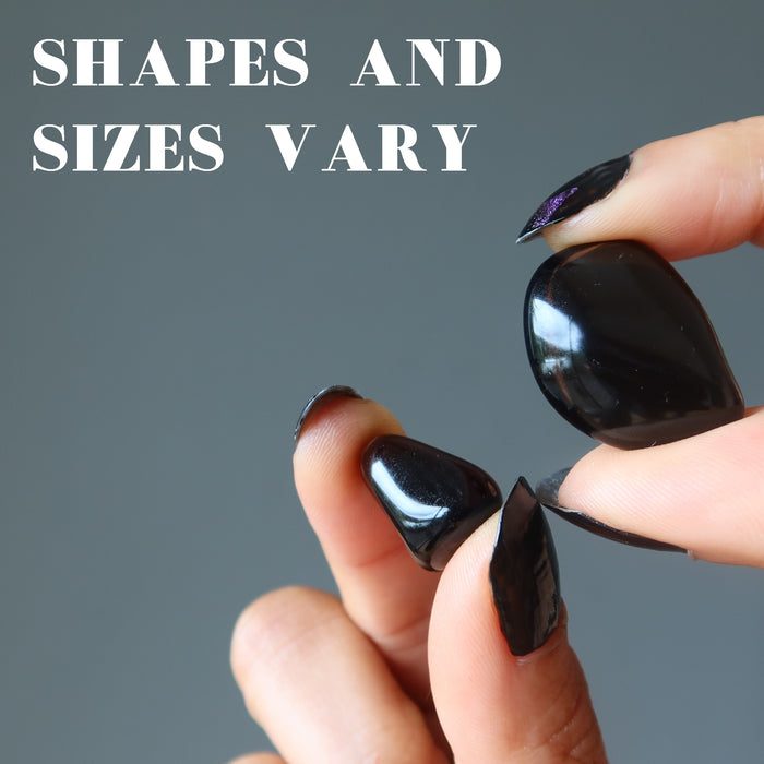 hand showing two different obsidian tumbled stones to show shapes and sizes vary