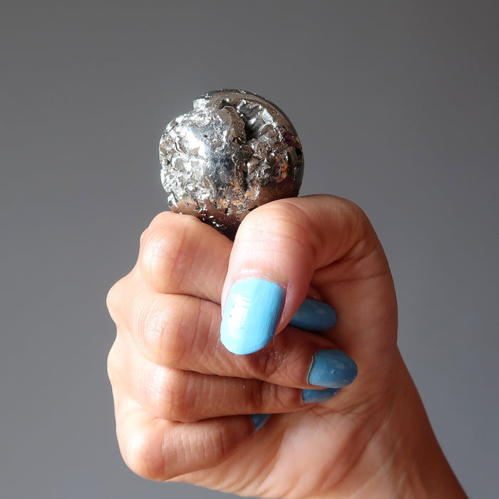 fist holding up gold pyrite geode sphere