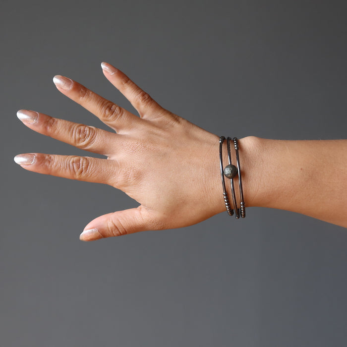 hand wearing a faceted pyrite on 3 coils of gunmetal beaded memory wire bracelet