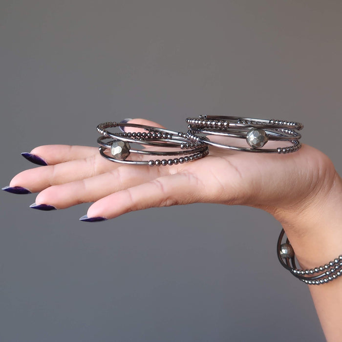 hand holding and wearing faceted pyrite on 3 coils of gunmetal beaded memory wire bracelets