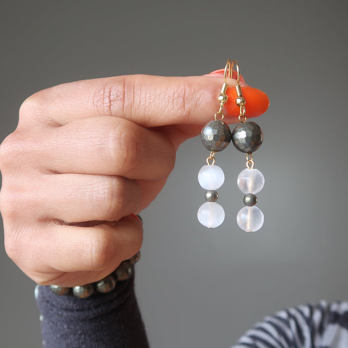 hands holding faceted pyrite and white selenite dangle earrings