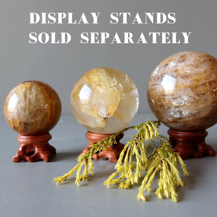 three golden quartz spheres on wood display stands and a sprig of pine 