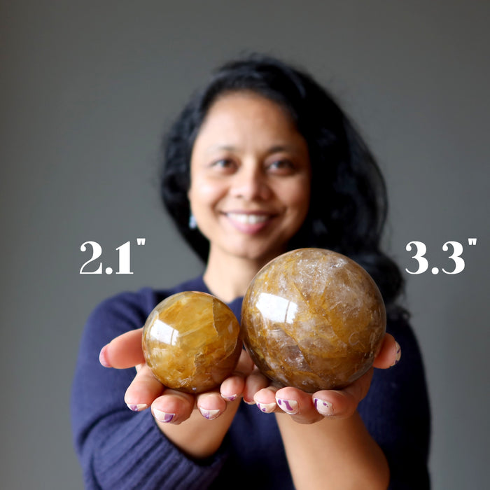 sheila of satin crystals holding a 2.1" and a 3.3" golden quartz sphere