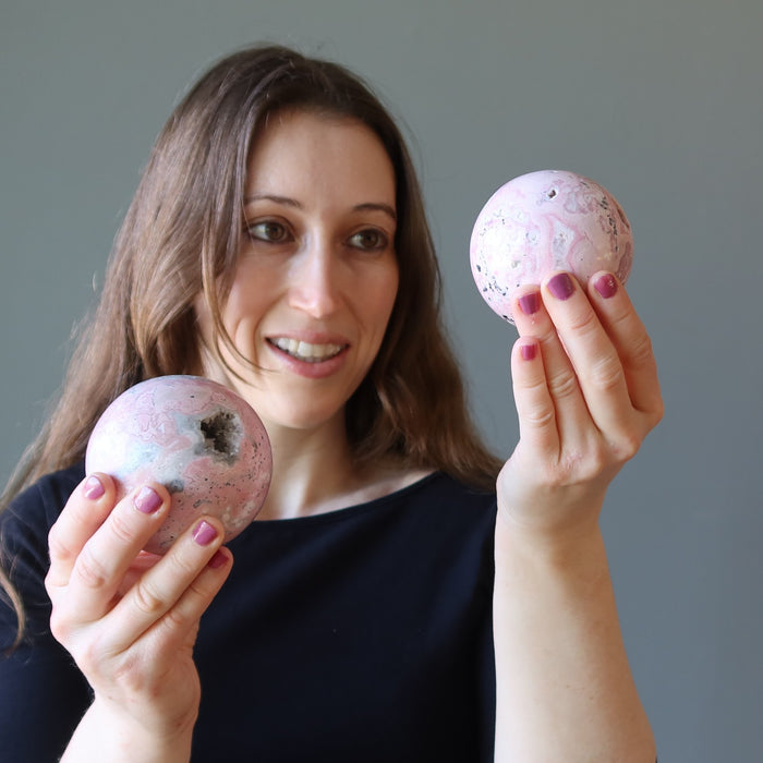 woman holding two rhodonite geode spheres