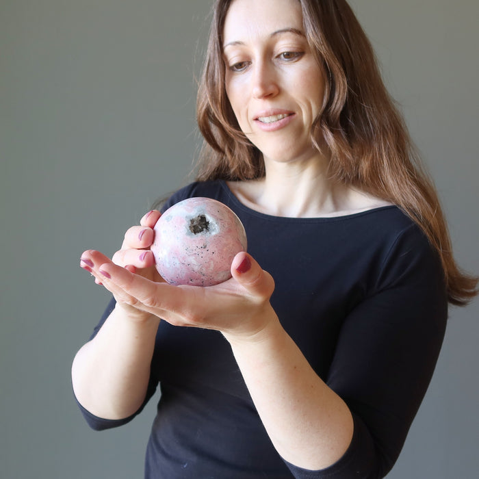 woman holding rhodonite geode sphere