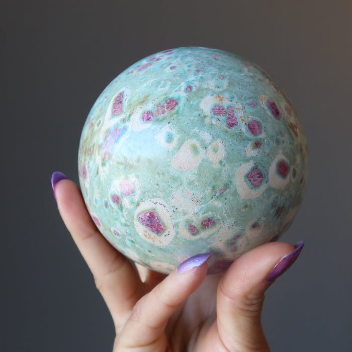 hand holding hand holding ruby fuchsite sphere