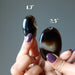 hand holding pair of black and brown sardonyx oval stones to show size difference