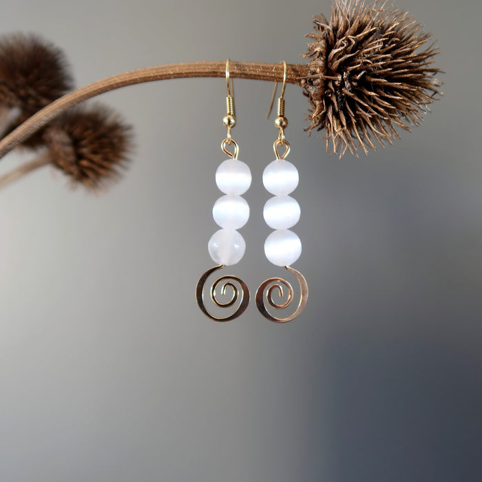 white selenite gold spiral dangle earrings hanging off a branch