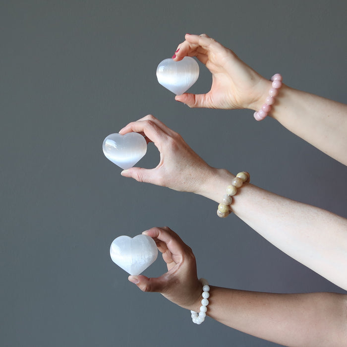 three hands holding set of three white selenite hearts