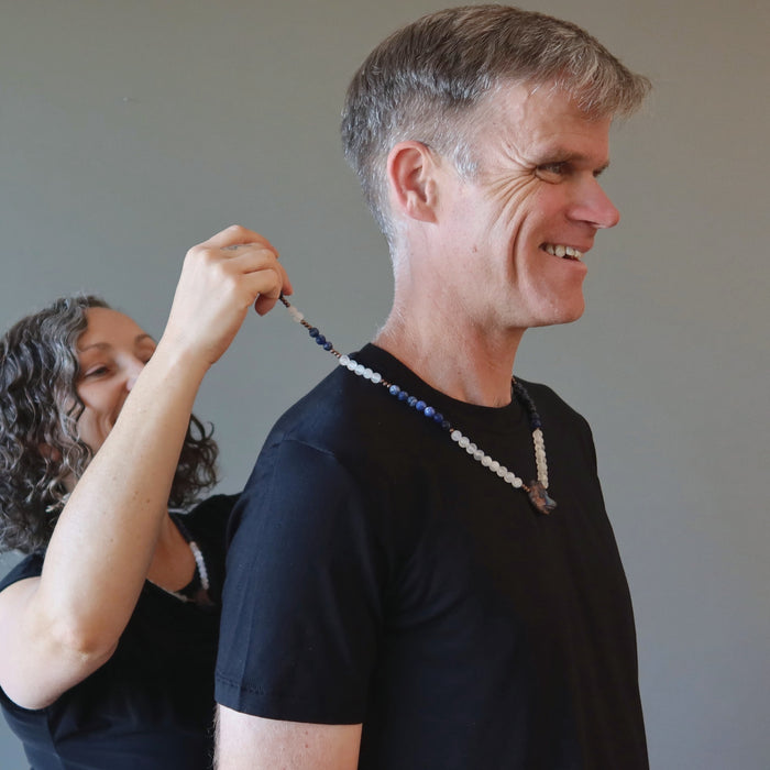 woman placing selenite sodalite wolf necklace on man