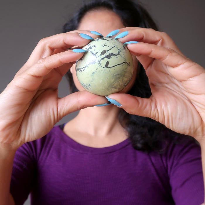 female holding a serpenting sphere in front of her face