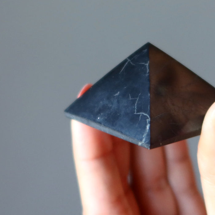 hand holding black shungite stone pyramid showing natural veins