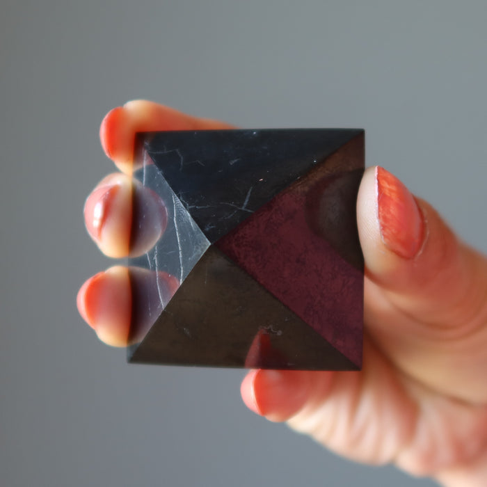 hand holding black shungite stone pyramid showing natural veins