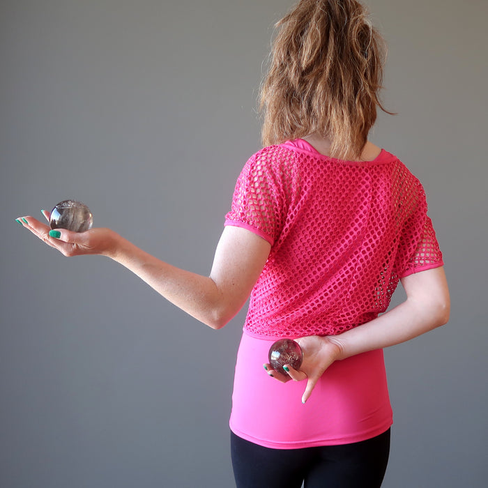 female with back turned posing with two smoky quartz spheres